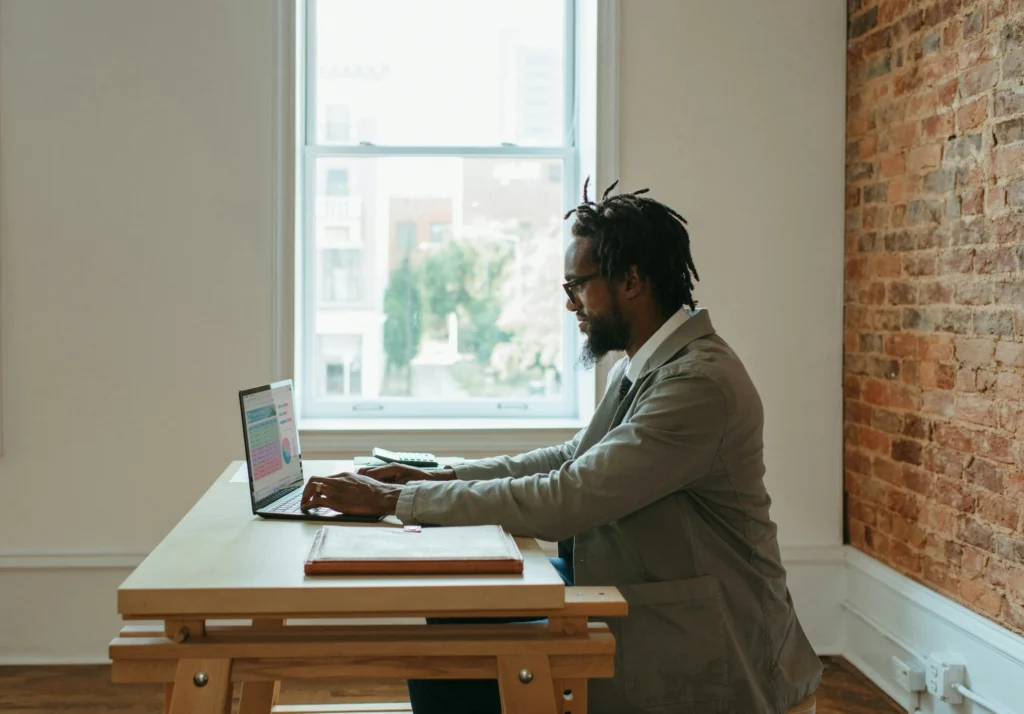 A professional working on a laptop at home with natural light, minimal distractions, and a calm environment.